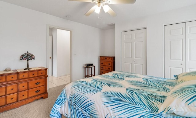 bedroom featuring two closets, light colored carpet, and ceiling fan