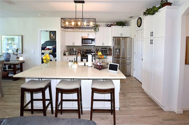 kitchen featuring appliances with stainless steel finishes, a kitchen breakfast bar, white cabinetry, backsplash, and light wood-style floors