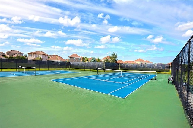 view of tennis court featuring fence and a residential view