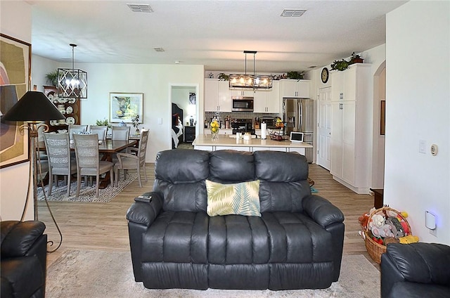 living area with a chandelier, light wood finished floors, and arched walkways