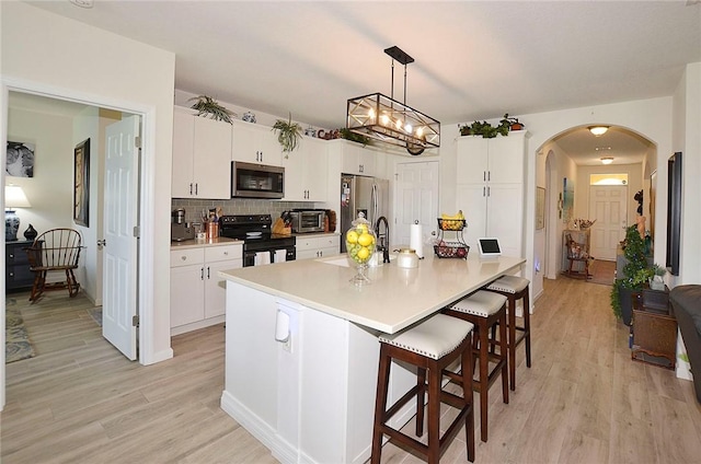 kitchen with appliances with stainless steel finishes, arched walkways, light wood-style floors, and a kitchen bar