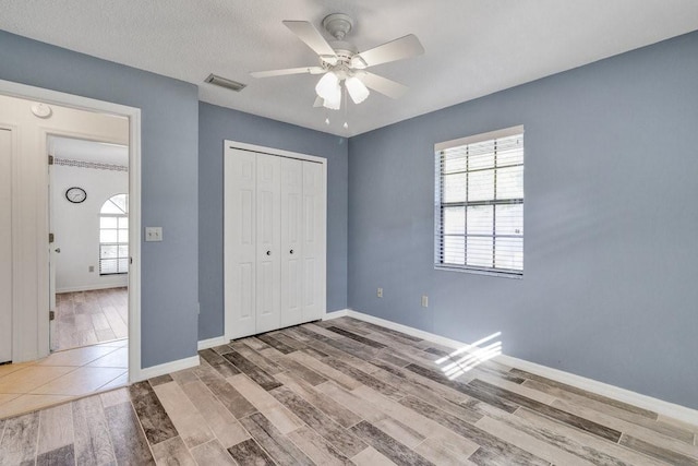 unfurnished bedroom featuring multiple windows, wood-type flooring, a closet, and ceiling fan