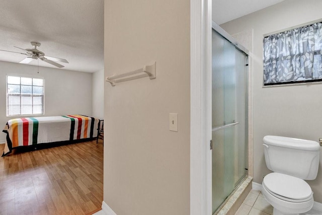 bathroom with ceiling fan, wood-type flooring, a shower with shower door, and toilet