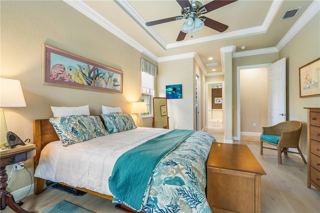 bedroom featuring ensuite bath, light wood-type flooring, ceiling fan, a tray ceiling, and crown molding