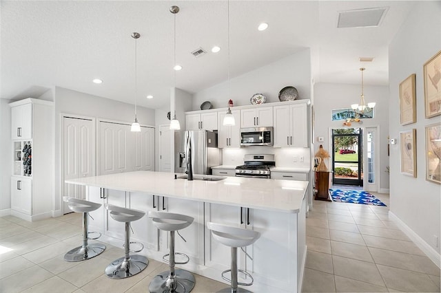 kitchen with stainless steel appliances, light tile patterned floors, a spacious island, white cabinets, and decorative light fixtures