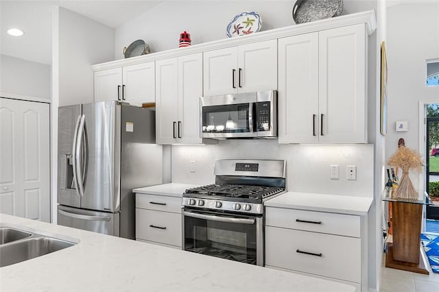 kitchen featuring light stone counters, tasteful backsplash, white cabinets, appliances with stainless steel finishes, and sink