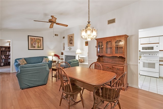 dining space featuring vaulted ceiling, light hardwood / wood-style flooring, and ceiling fan with notable chandelier