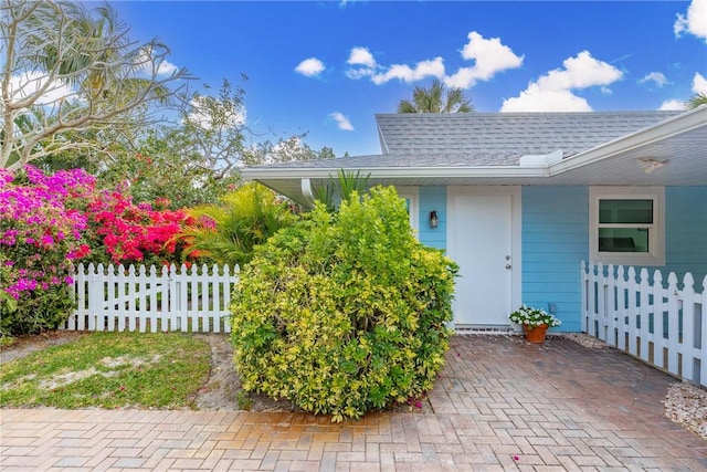 doorway to property with a shingled roof and fence