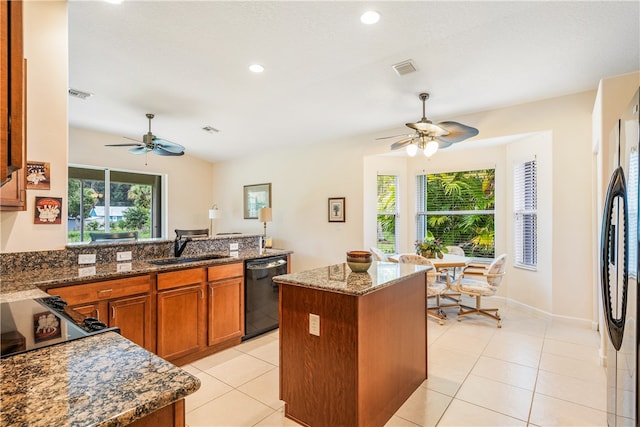 kitchen featuring dishwasher, dark stone counters, sink, a kitchen island, and stainless steel refrigerator