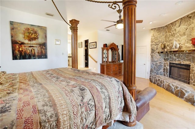 bedroom with visible vents, a stone fireplace, ornate columns, and wood finished floors