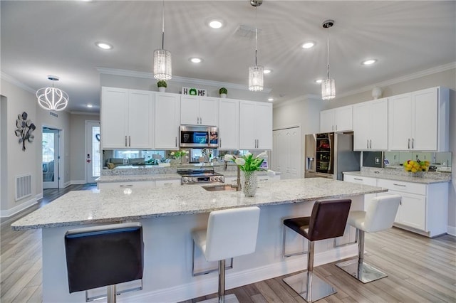 kitchen featuring a large island with sink, appliances with stainless steel finishes, decorative light fixtures, a kitchen bar, and white cabinetry