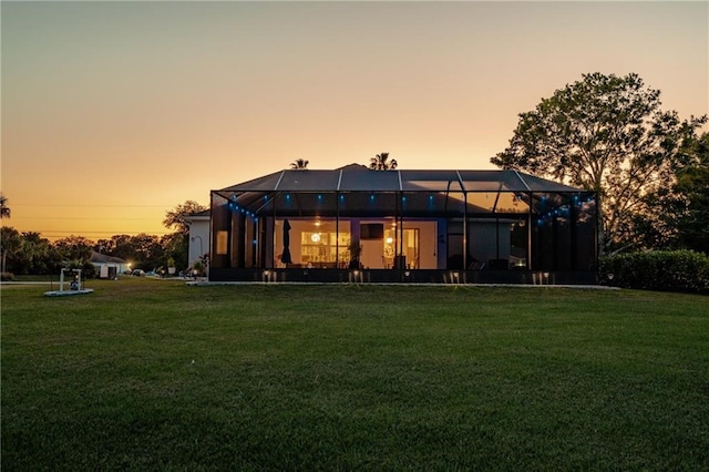 back house at dusk with glass enclosure and a yard