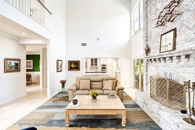 tiled living area featuring a high ceiling, a brick fireplace, visible vents, and baseboards