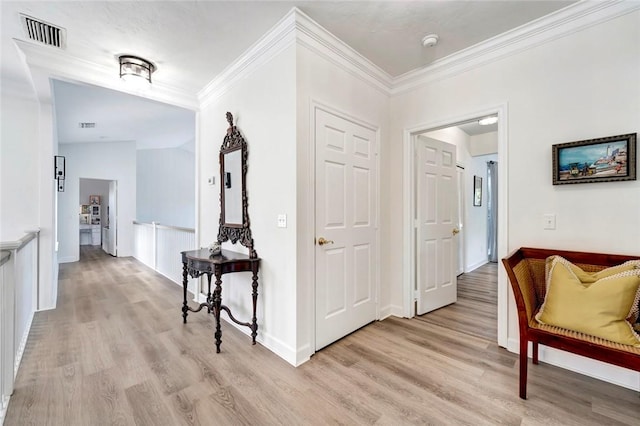 hallway with visible vents, light wood-style floors, and ornamental molding