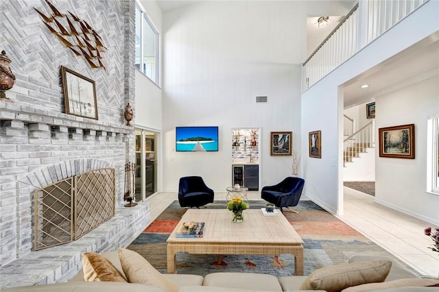 tiled living area featuring visible vents, baseboards, a brick fireplace, a towering ceiling, and stairs