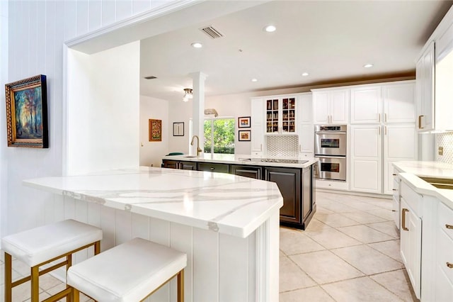 kitchen with stainless steel double oven, backsplash, a peninsula, and an island with sink