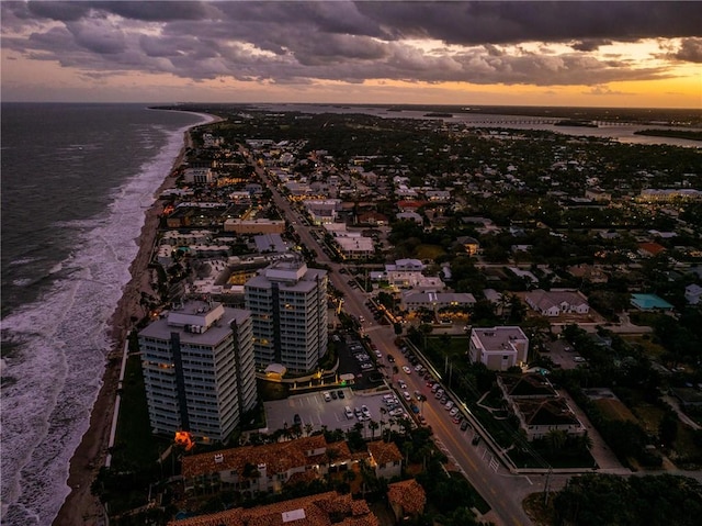 aerial view at dusk featuring a water view and a beach view