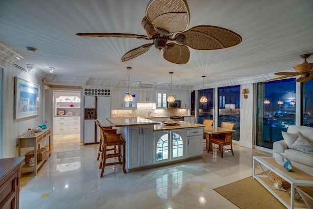 kitchen featuring ceiling fan, light stone countertops, decorative backsplash, a kitchen island, and decorative light fixtures