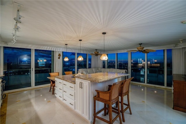 kitchen featuring white cabinetry, hanging light fixtures, a center island, floor to ceiling windows, and light stone countertops