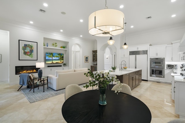 dining space featuring a notable chandelier, crown molding, built in features, and sink