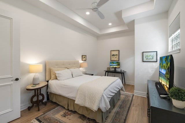 bedroom with ceiling fan, a raised ceiling, and hardwood / wood-style floors