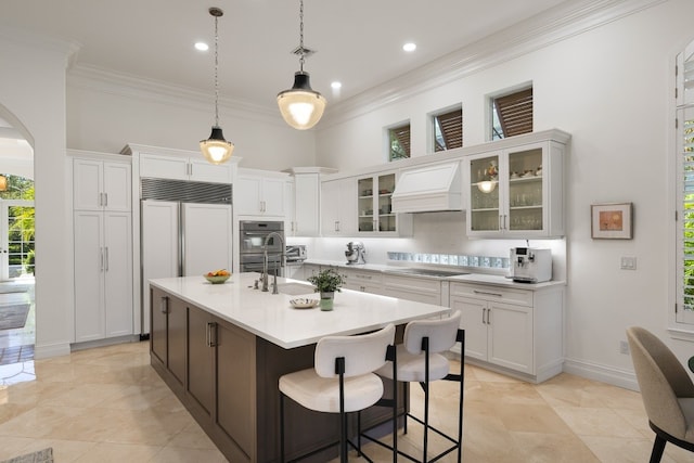 kitchen featuring custom exhaust hood, paneled refrigerator, white cabinetry, and an island with sink