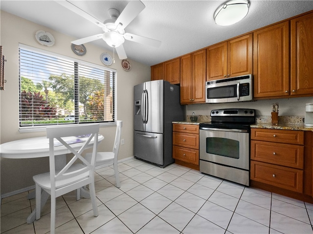 kitchen with light stone countertops, ceiling fan, light tile patterned floors, and appliances with stainless steel finishes