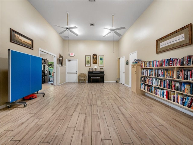 misc room with light hardwood / wood-style flooring, ceiling fan, and a towering ceiling