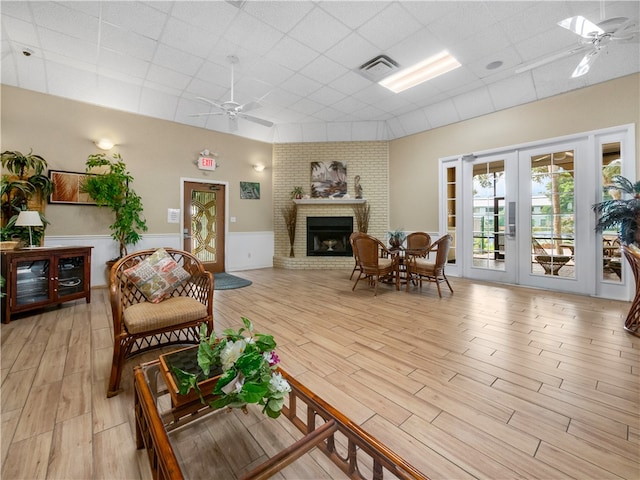 living room featuring french doors, a brick fireplace, a drop ceiling, ceiling fan, and light hardwood / wood-style flooring