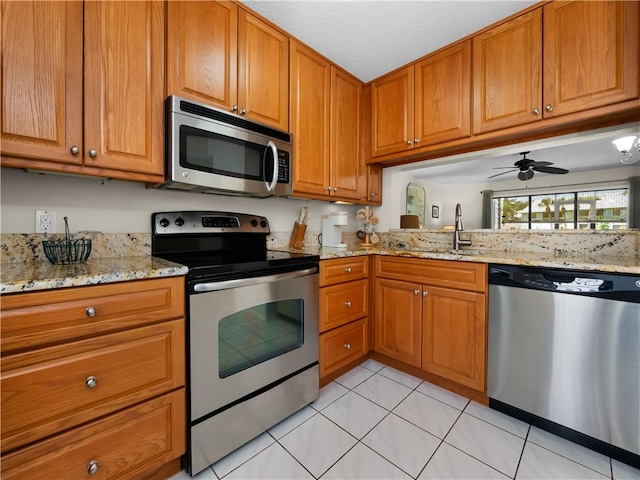 kitchen featuring light tile patterned flooring, appliances with stainless steel finishes, light stone countertops, sink, and ceiling fan