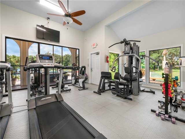 exercise room with a towering ceiling, ceiling fan, and plenty of natural light