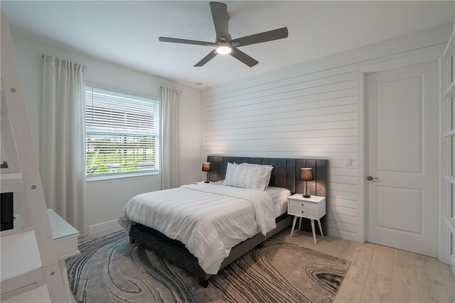 bedroom with ceiling fan, light hardwood / wood-style floors, and wooden walls