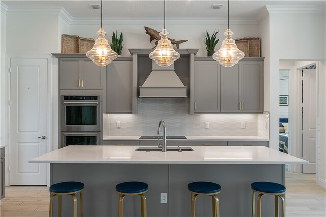 kitchen featuring decorative light fixtures, gray cabinets, custom exhaust hood, decorative backsplash, and double oven