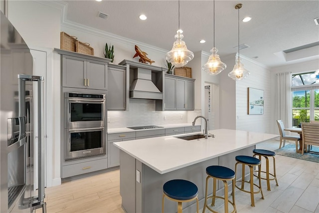 kitchen with gray cabinets, appliances with stainless steel finishes, decorative light fixtures, custom range hood, and sink