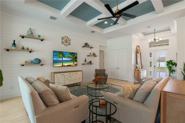 living room with ceiling fan with notable chandelier, beamed ceiling, wood walls, light wood-type flooring, and coffered ceiling