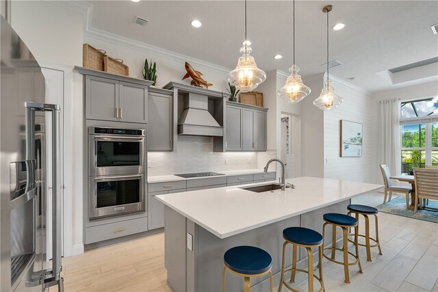 kitchen with custom exhaust hood, stainless steel appliances, sink, hanging light fixtures, and gray cabinetry