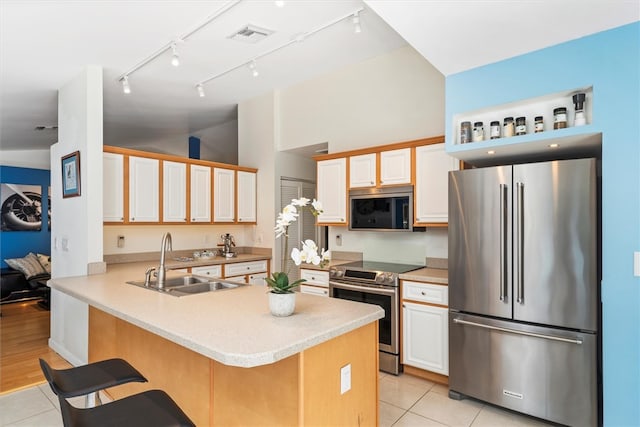 kitchen featuring sink, light tile patterned floors, appliances with stainless steel finishes, a kitchen bar, and kitchen peninsula