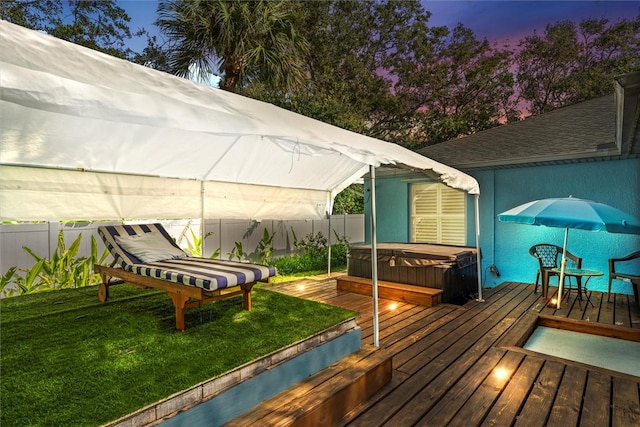 deck at dusk with a yard and a hot tub