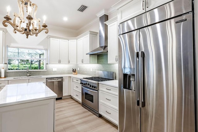 kitchen with sink, hanging light fixtures, high quality appliances, wall chimney range hood, and white cabinets