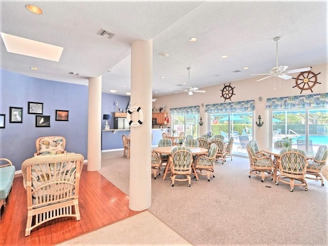 dining area with a textured ceiling, wood-type flooring, ceiling fan, and a skylight