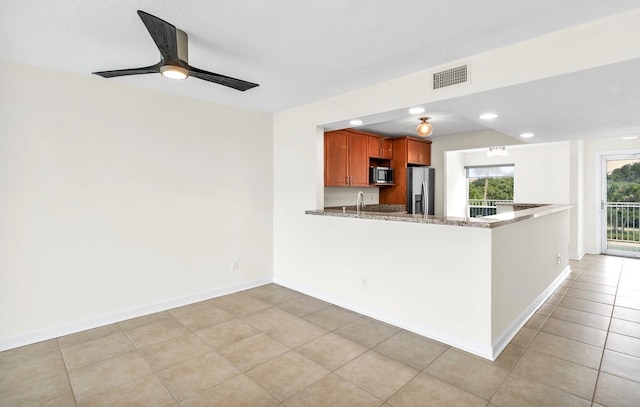 kitchen with kitchen peninsula, light tile patterned floors, sink, light stone countertops, and appliances with stainless steel finishes