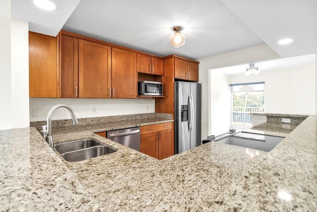 kitchen with a textured ceiling, sink, light stone counters, and appliances with stainless steel finishes