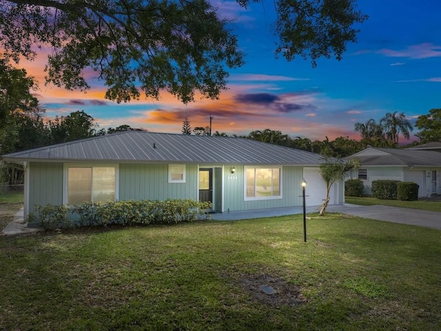 ranch-style home with driveway, an attached garage, metal roof, and a lawn