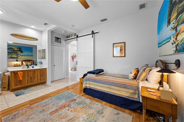 bedroom featuring ceiling fan, a barn door, light tile patterned floors, and ensuite bath