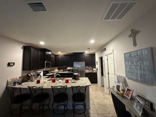 kitchen featuring a kitchen bar, stainless steel appliances, light stone counters, kitchen peninsula, and light tile patterned floors