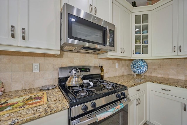 kitchen with stainless steel appliances, tasteful backsplash, glass insert cabinets, and white cabinetry