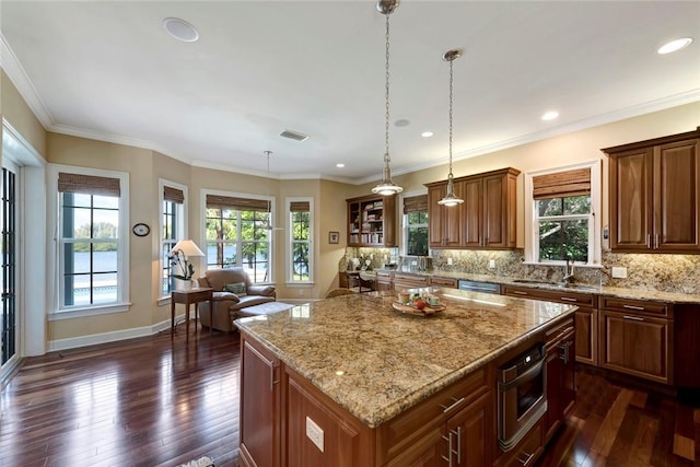 kitchen with light stone countertops, hanging light fixtures, dark hardwood / wood-style flooring, crown molding, and a kitchen island