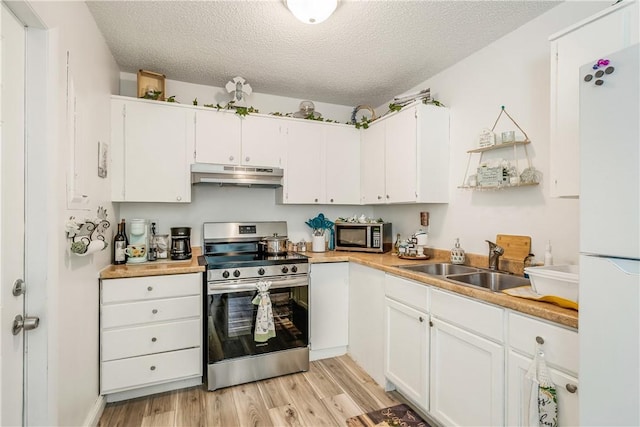 kitchen with appliances with stainless steel finishes, a sink, a textured ceiling, light wood-type flooring, and under cabinet range hood