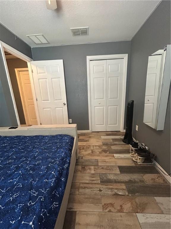bedroom with wood finished floors, a textured ceiling, visible vents, a ceiling fan, and baseboards