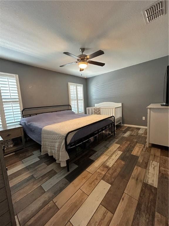 bedroom featuring ceiling fan, a textured ceiling, visible vents, and wood finished floors